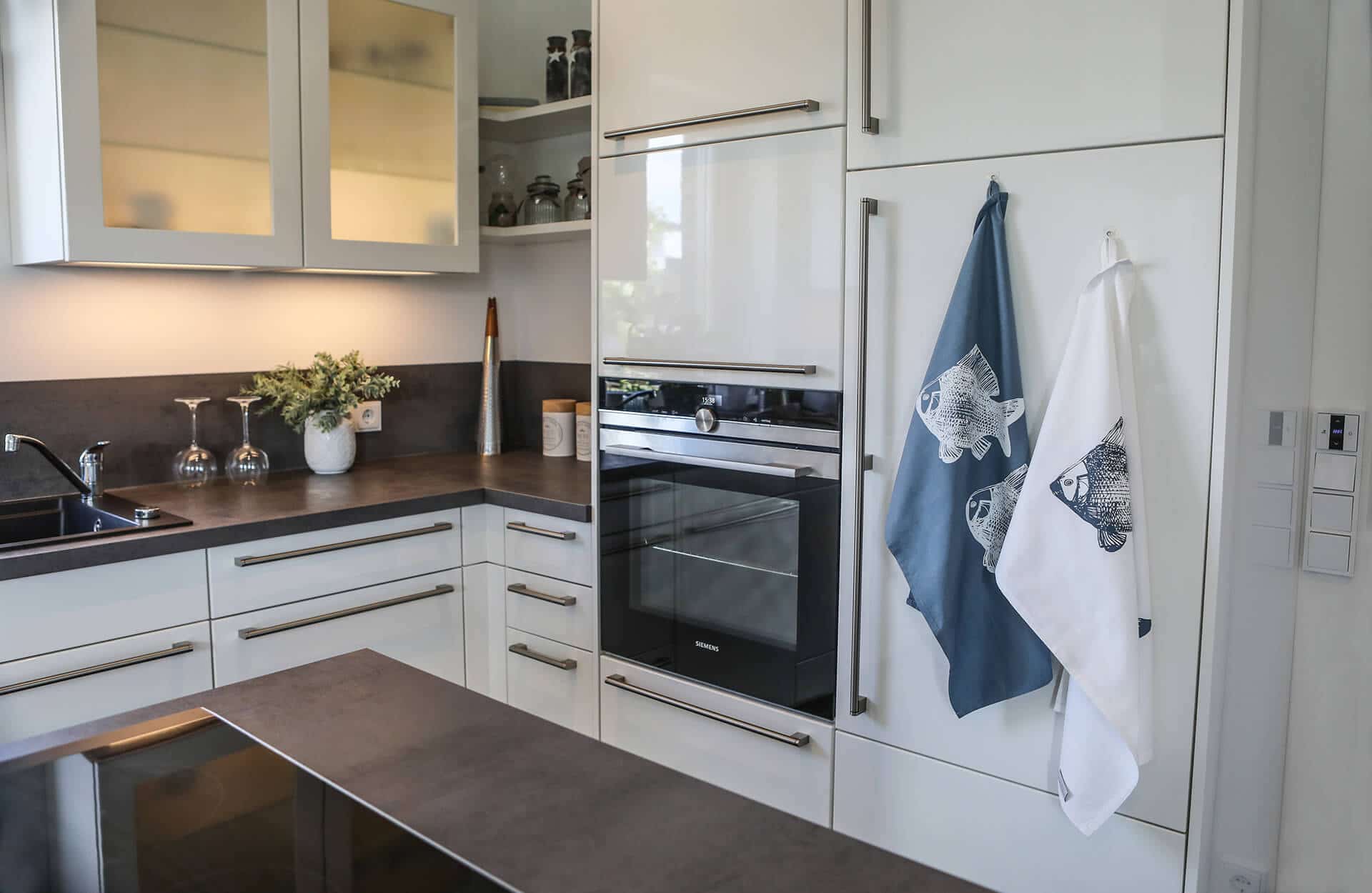 Zwei Geschirrtücher in der Farbe blaugrau und weiß mit Fischmotiv hängen an einem Kühlschrank.