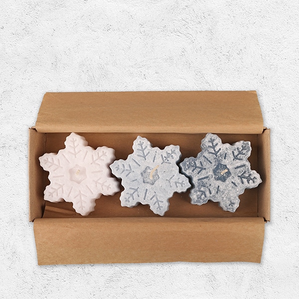 Drei Schwimmkerzen in Form von Schneekristallen in einer Verpackung aus Pappe.