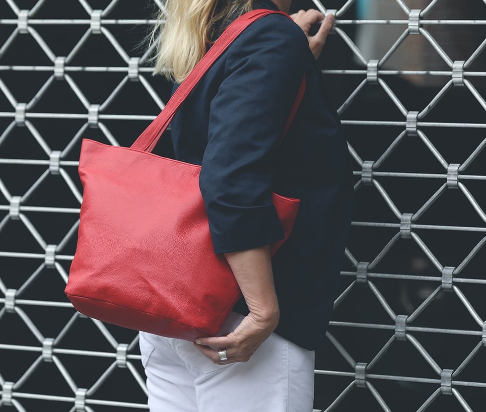 Eine Person trägt eine Handtasche aus Leder in der Farbe corallrot über der Schulter.