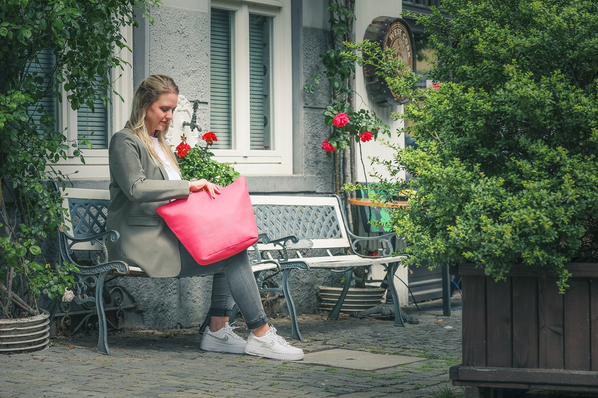 Eine Person sitzt auf einer Bank und schaut in eine Handtasche aus Leder in der Farbe fleuro, einem Rosaton.