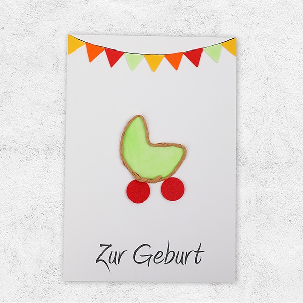 Eine Karte mit bunten Fähnchen und einer Wiege in grün mit der Aufschrift Zur Geburt.