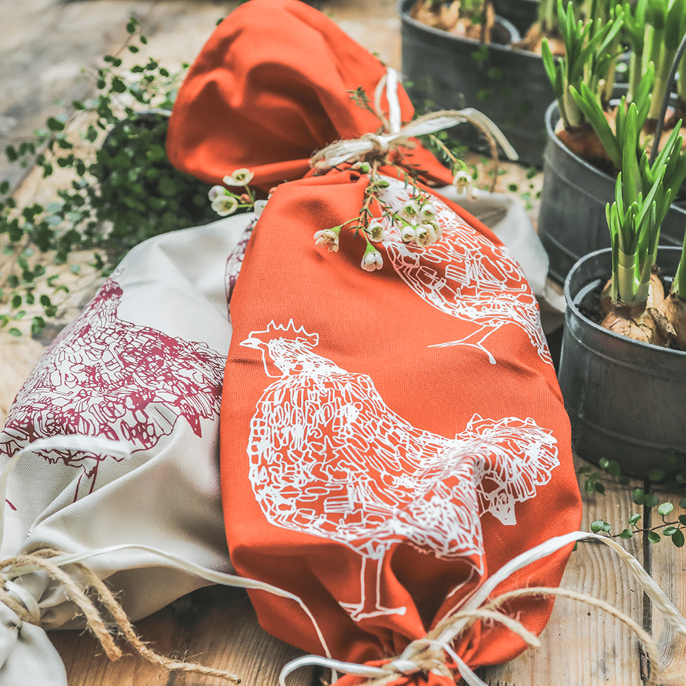 Geschirrtuch mit Hühnermotiv, in beige und rost-orange in Geschenkform, mit Pflanzen dekoriert.