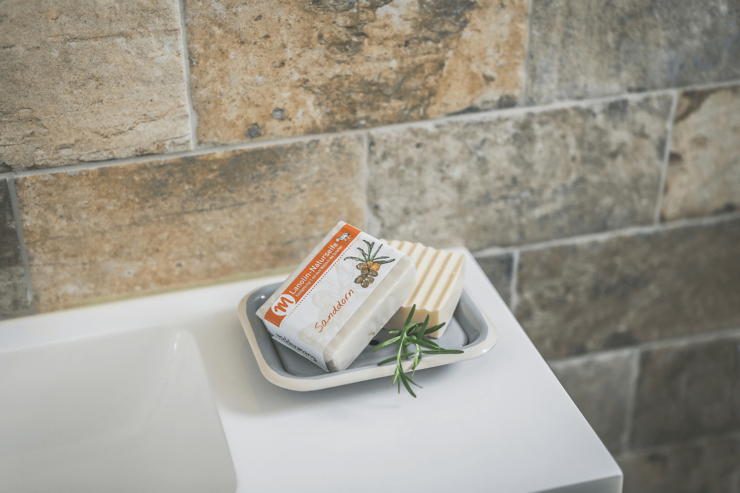 Zwei Stücke Lanolin-Naturseife Sanddorn liegen auf einer Seifenschale.