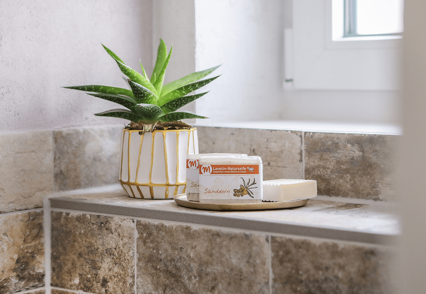 Zwei Stücke Lanolin-Naturseife Sanddorn stehen auf einer Seifenschale.