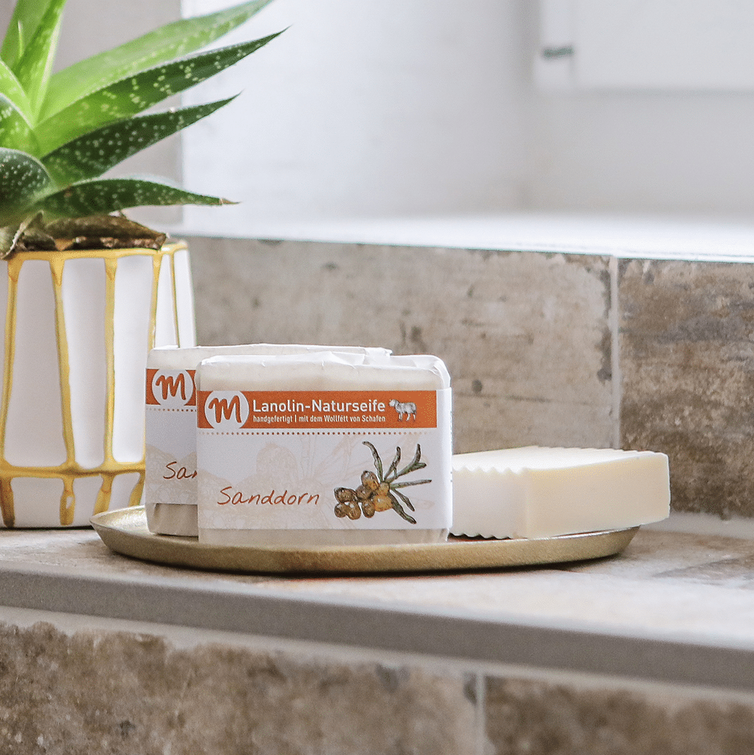 Drei Stücke Lanolin-Naturseife mit Sanddorn befinden sich auf einem goldfarbenen Tablett.