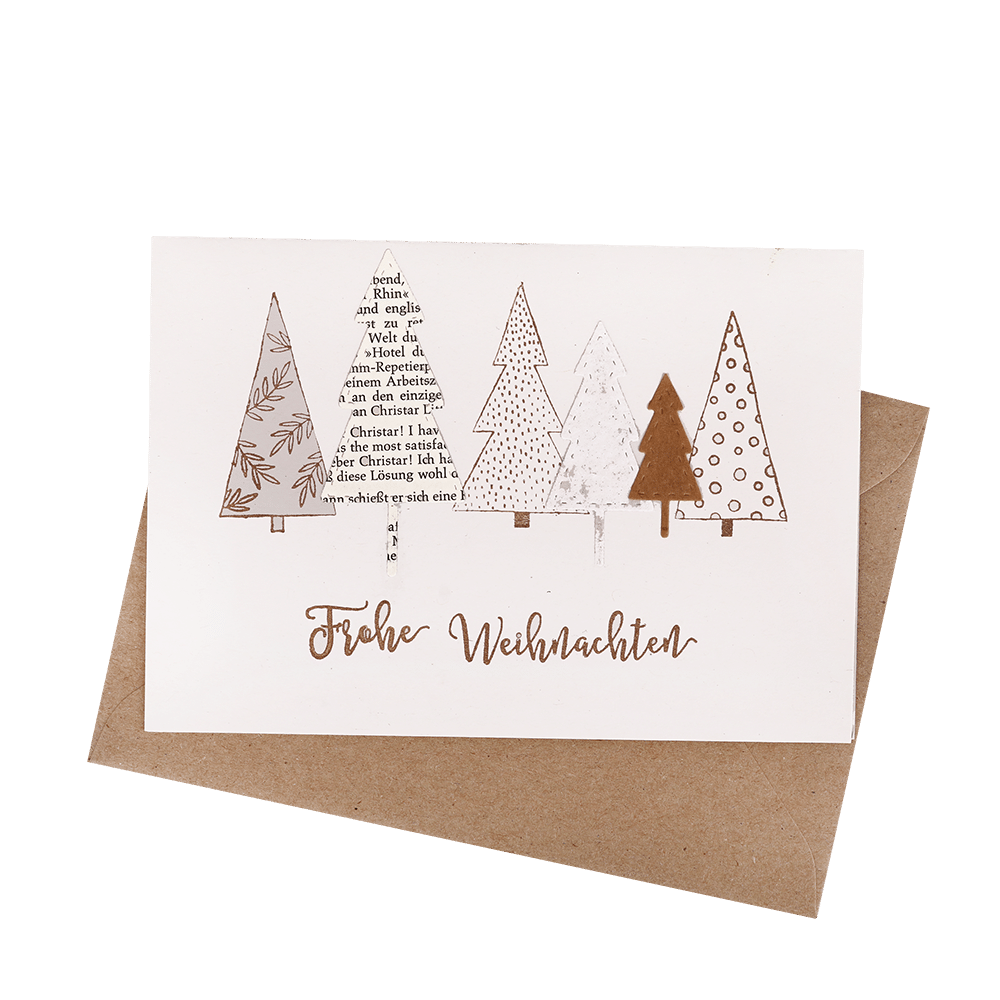 Handgefertigte Klappkarte mit aufgeklebten Tannenbäumen aus Papier und dem Spruch Frohe Weihnachten, mit braunem Umschlag.