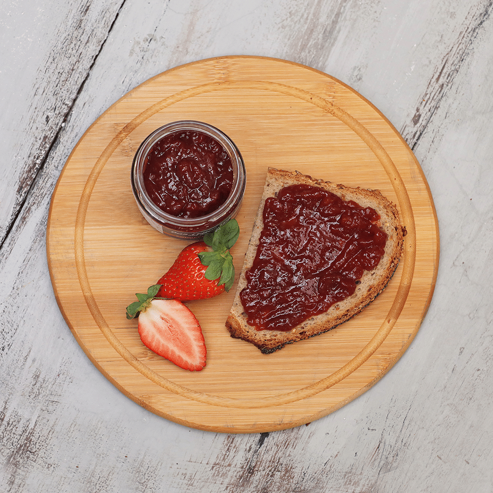 Fruchtaufstrich in Erdbeer auf Brot auf rundem Holzbrett.