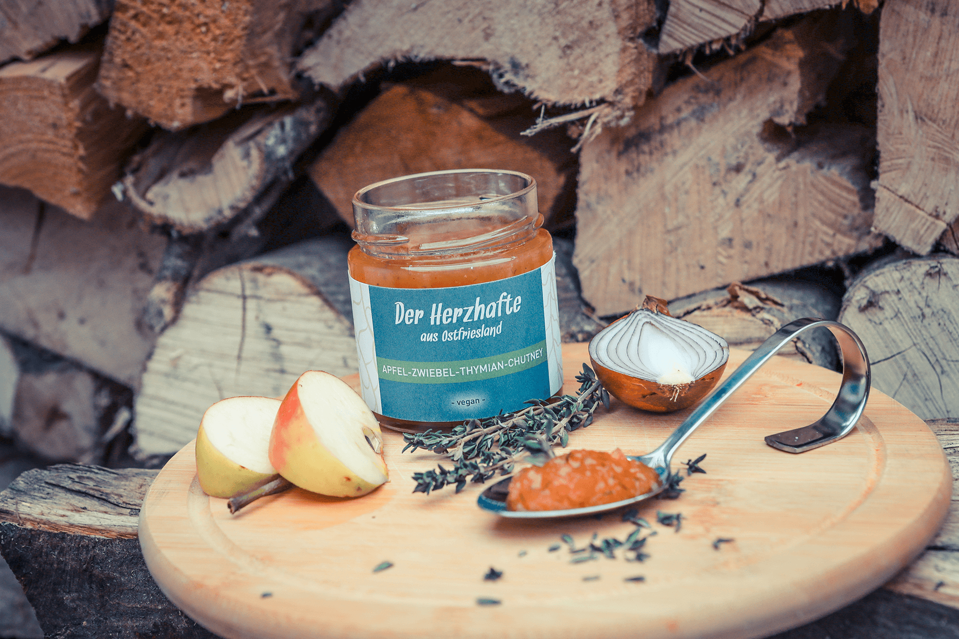 Apfel-Zwiebel-Thymian-Chutney dekoriert mit Apfelspalten, Zwiebelhälfte und Thymianzweig auf Holzbrett.