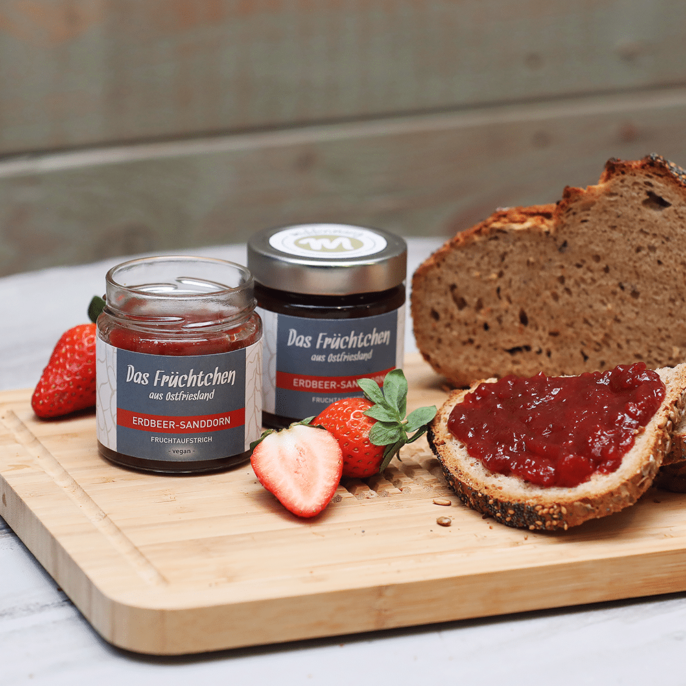 Fruchtaufstrich das Früchtchen in Erdbeer-Sanddorn auf Holzbrett mit Brot und Erdbeeren.