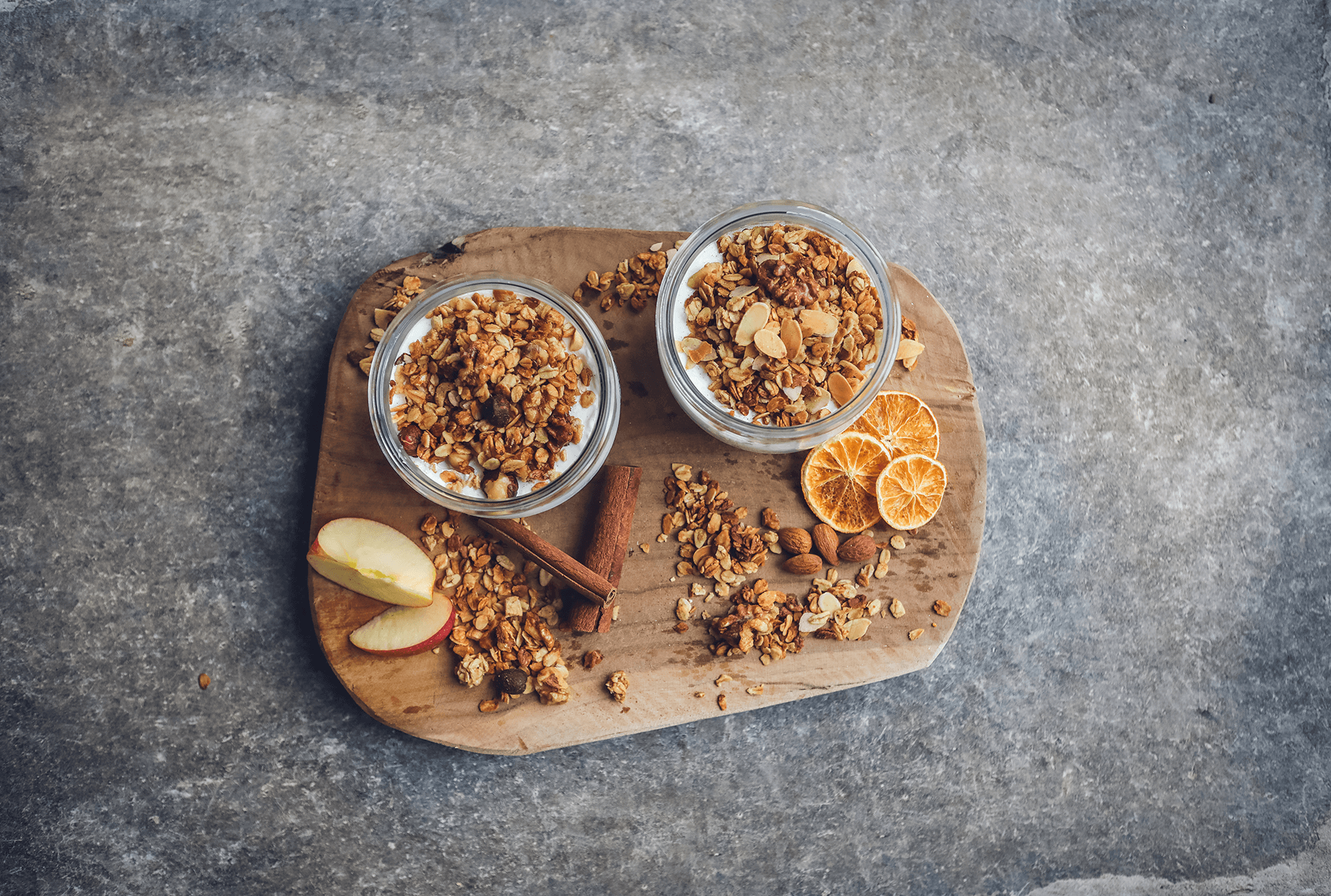 Knuspermüsli mit Apfel-Zimt und Mandel-Orange-Spekulatius auf Holzbrett in Glasschälchen angerichtet.