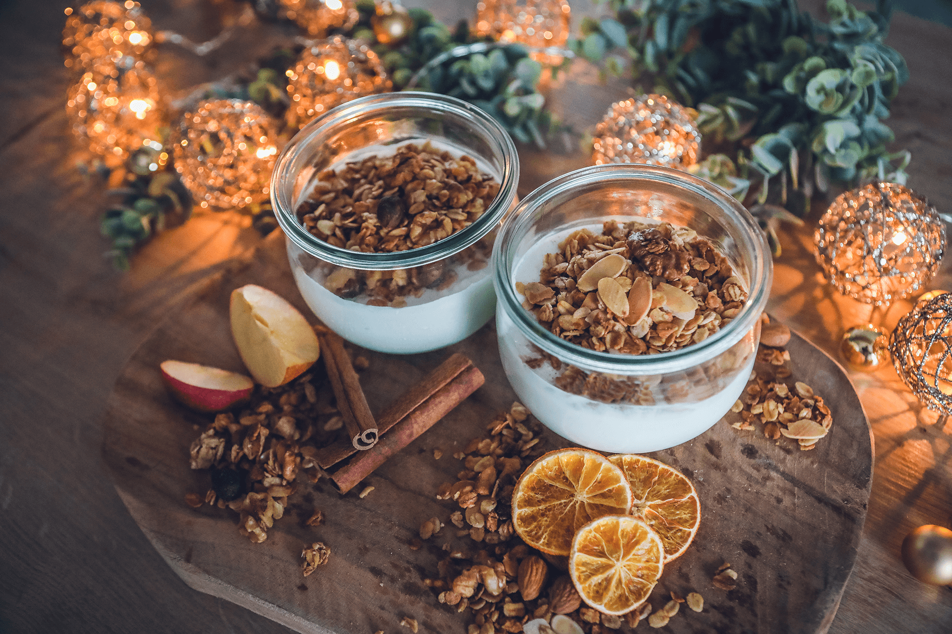 Knuspermüsli mit Apfel-Zimt und Mandel-Orange-Spekulatius auf Holzbrett in Glasschälchen angerichtet.