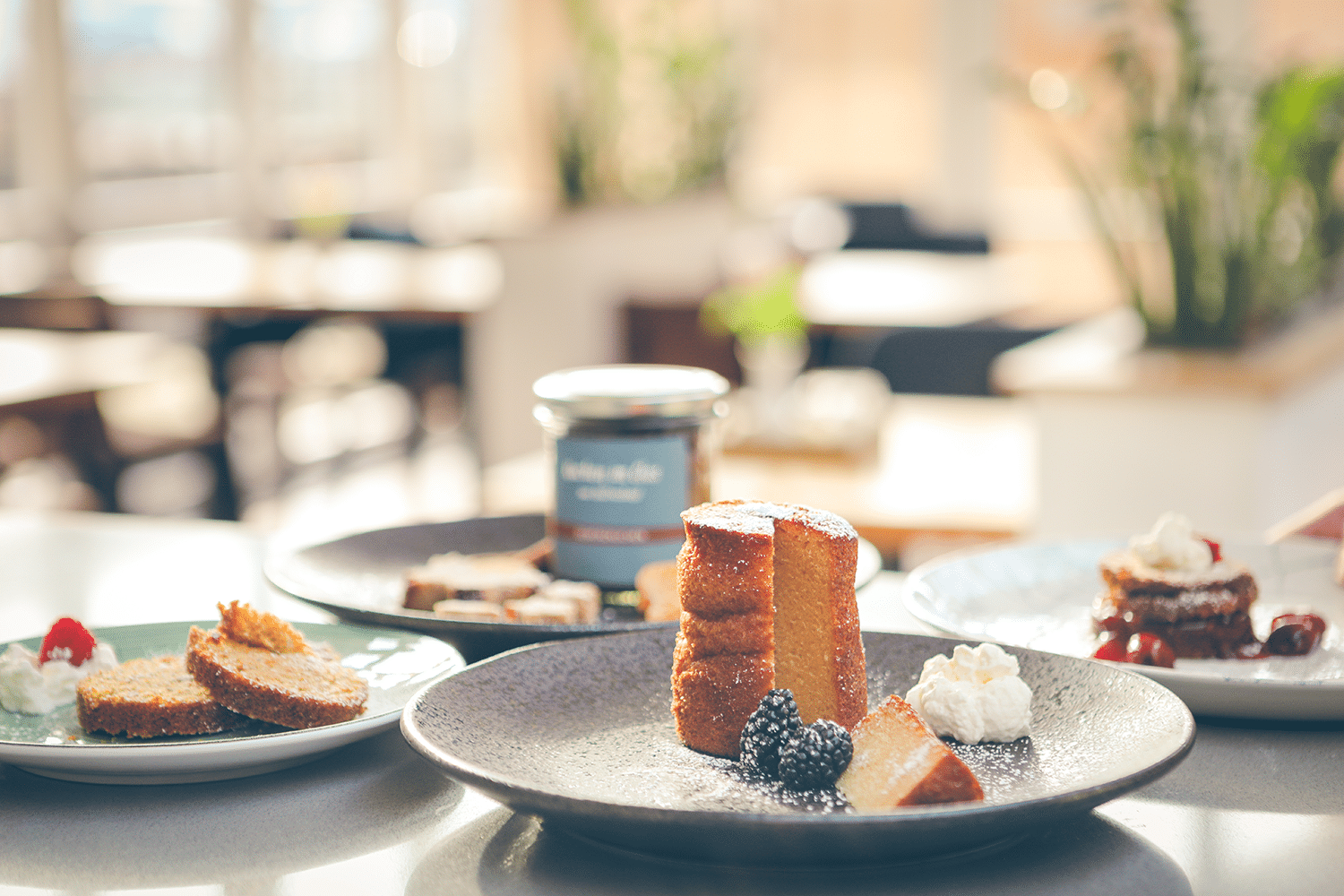 Drei Sorten Kuchen im Glas, auf drei Tellern mit Früchten, Puderzucker und Sahne angerichtet.