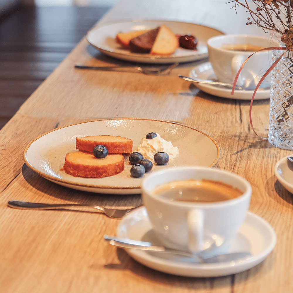Eierlikörkuchen, auf einer Kaffeetafel, angeschnitten und auf einem Teller angerichtet, mit Puderzucker, Sahne und Beeren.