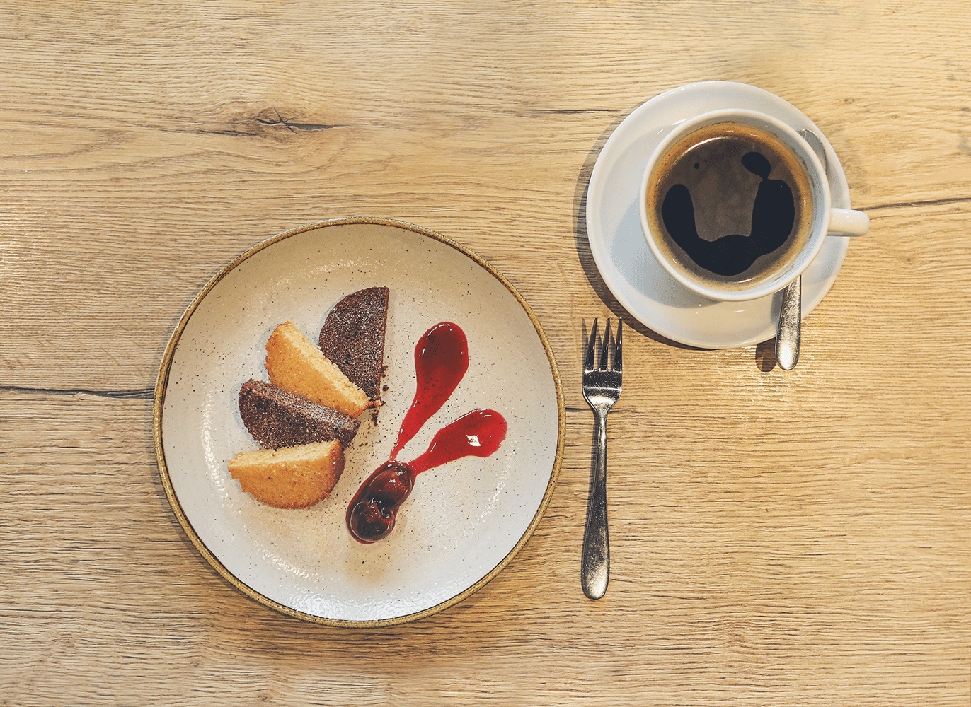 Kuchen im Glas, in Scheiben geschnitten und halbiert, auf einen Teller angerichtet, mit Kirschen und einer Tasse Kaffee.