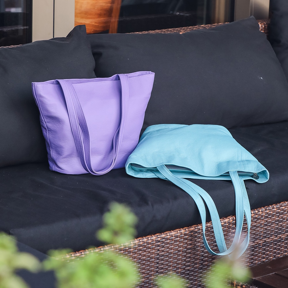 Zwei Taschen aus Leder in den Farben lila und türkis auf einer Gartenbank.