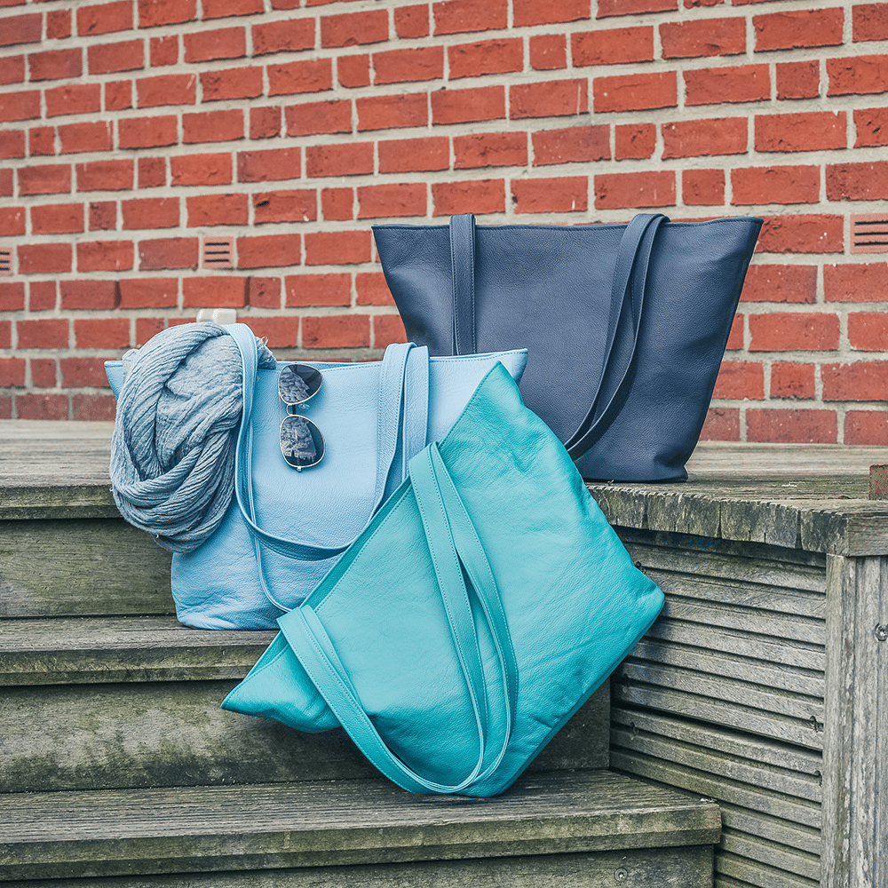 Drei Handtaschen aus Leder in verschiedenen Blautönen stehen auf Holztreppe.