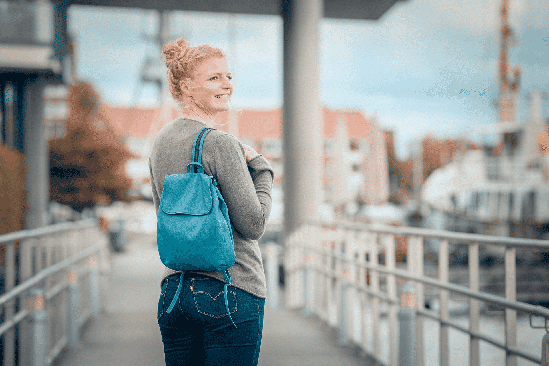 Eine Person trägt einen kleinen Rucksack aus Leder in der Farbe rauchblau auf dem Rücken.
