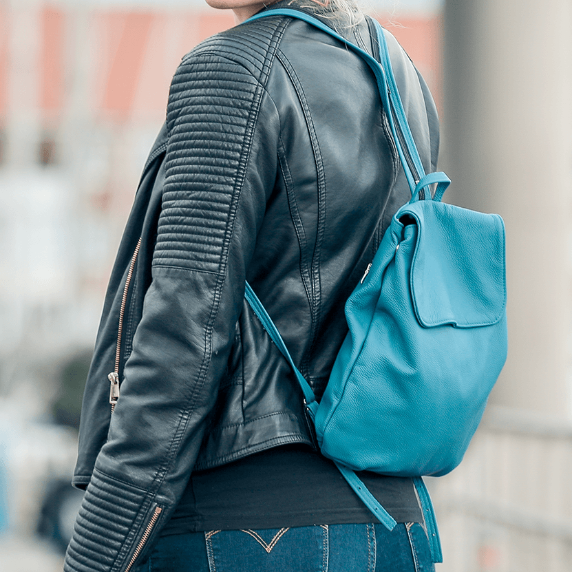 Eine Person trägt einen kleinen Rucksack aus Leder in der Farbe rauchblau auf dem Rücken.