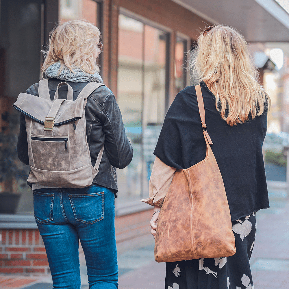 Zwei Personen bei einem Spaziergang mit dem Leder-Rucksack in beige und der Leder-Beuteltasche in hellbraun.