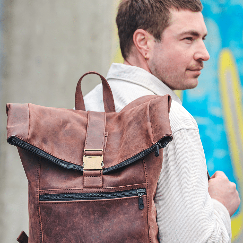 Person trägt Leder-Rucksack in braun auf der Schulter.