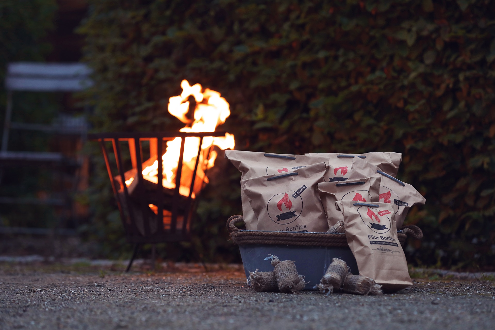 Ein brennender Feuerkorb in einem Garten, davor Anzünder Füür Bontjes.