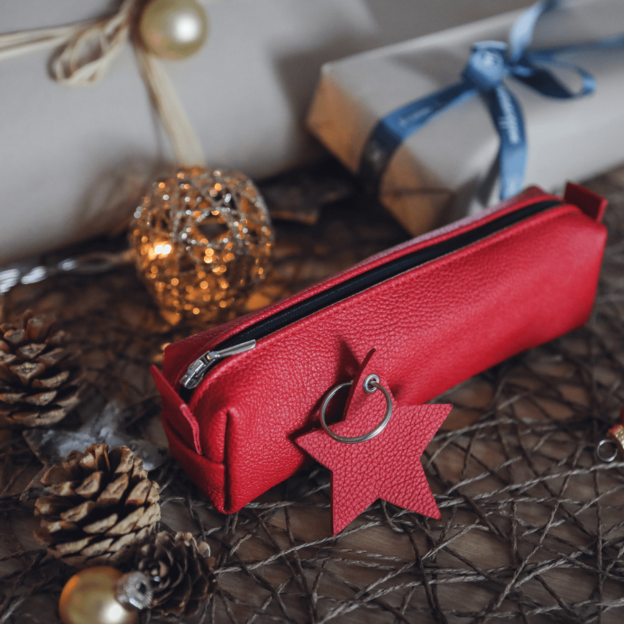 middenmang Faulenzer in rot, mit Schlüsselanhänger Stern in rot, dekoriert zwischen weihnachtlich verpackten Geschenken, Zapfen und Kugeln