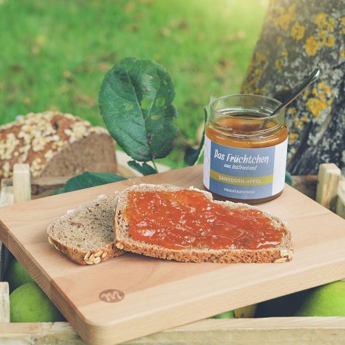 Fruchtaufstrich in Glasbehälter in Geschmacksrichtung Sanddorn-Apfel im Garten auf Holzbrettchen mit Brote mit Fruchtaufstrich.