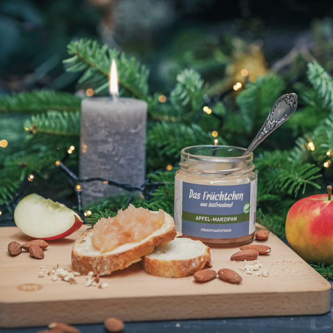 Ein Glas Fruchtaufstrich Pflaume Marzipan steht auf einem Brotbrett, dekoriert mit Marzipan und Pflaumen.