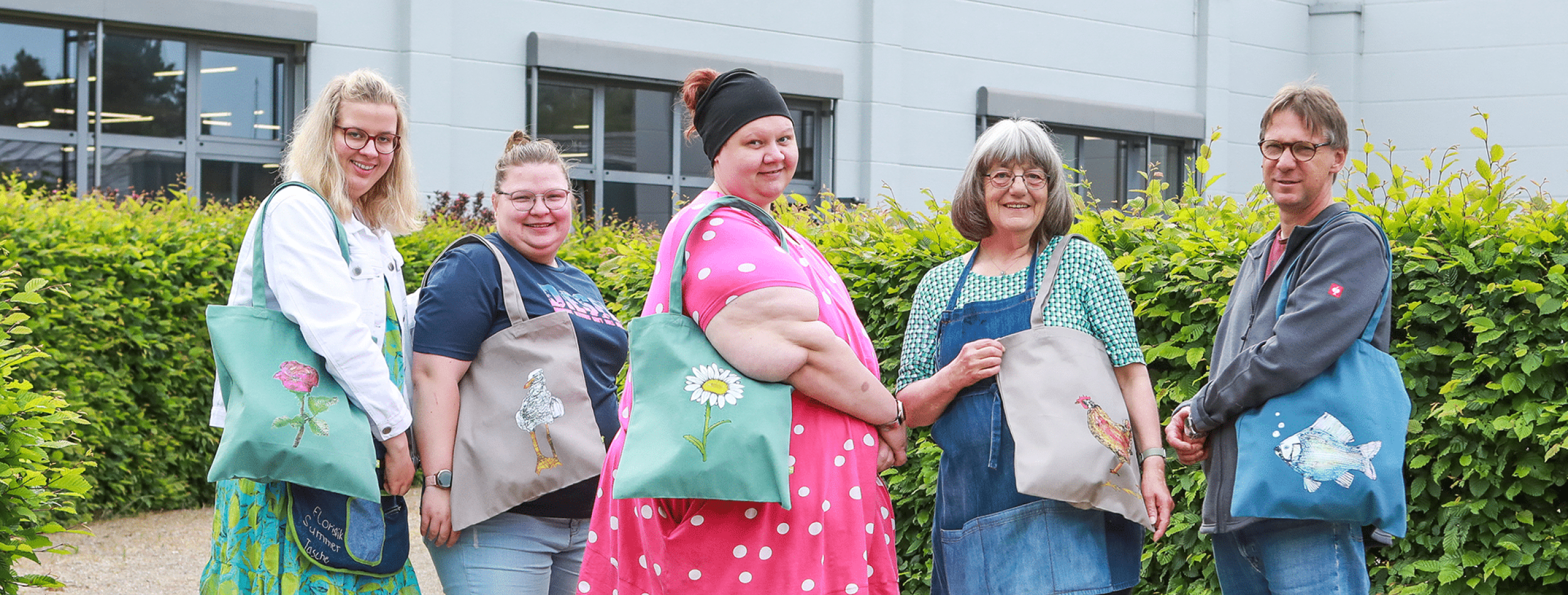Fünf Personen tragen Stofftaschen mit unterschiedlichen Motiven über der Schulter.