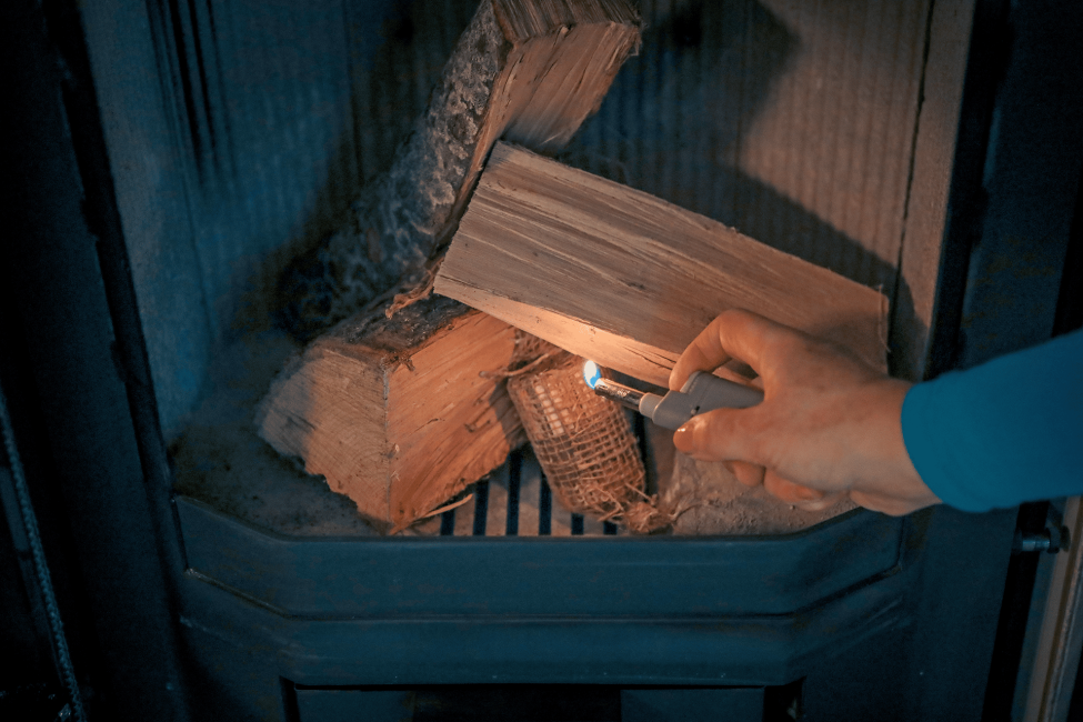 Anzünder Füür Bontjes in einem Kamin mit Holzscheiten, die gerade durch eine Person entzündet werden.